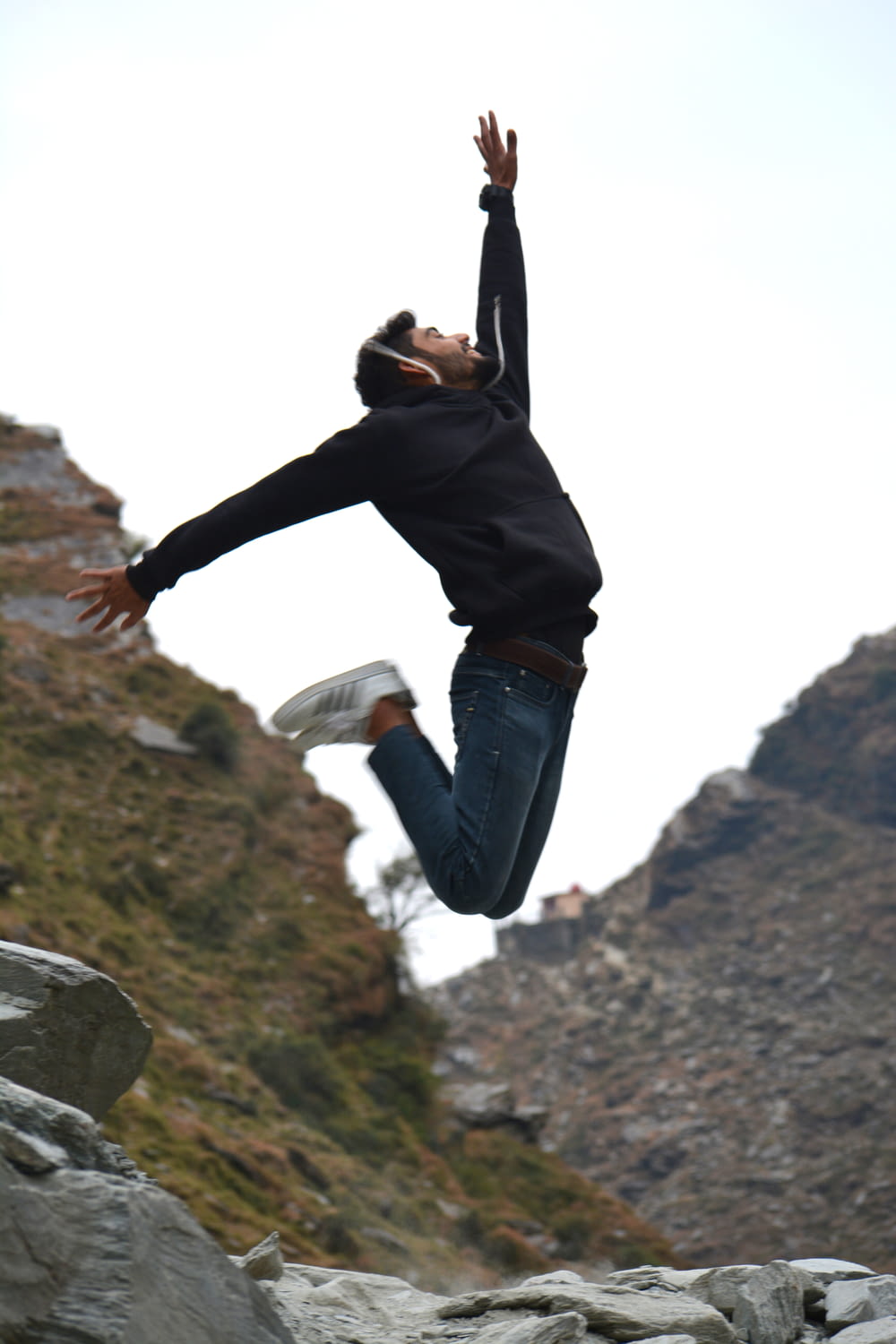 woman in black jacket and black pants jumping on gray rock during daytime