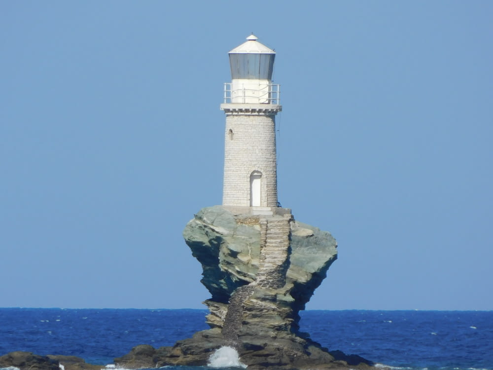 white and brown lighthouse on brown rock formation near sea during daytime