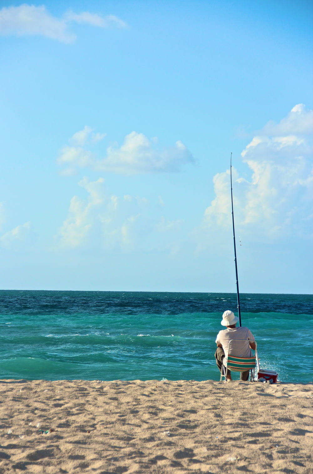 homem na camiseta branca sentado no banco de madeira marrom na praia durante o dia