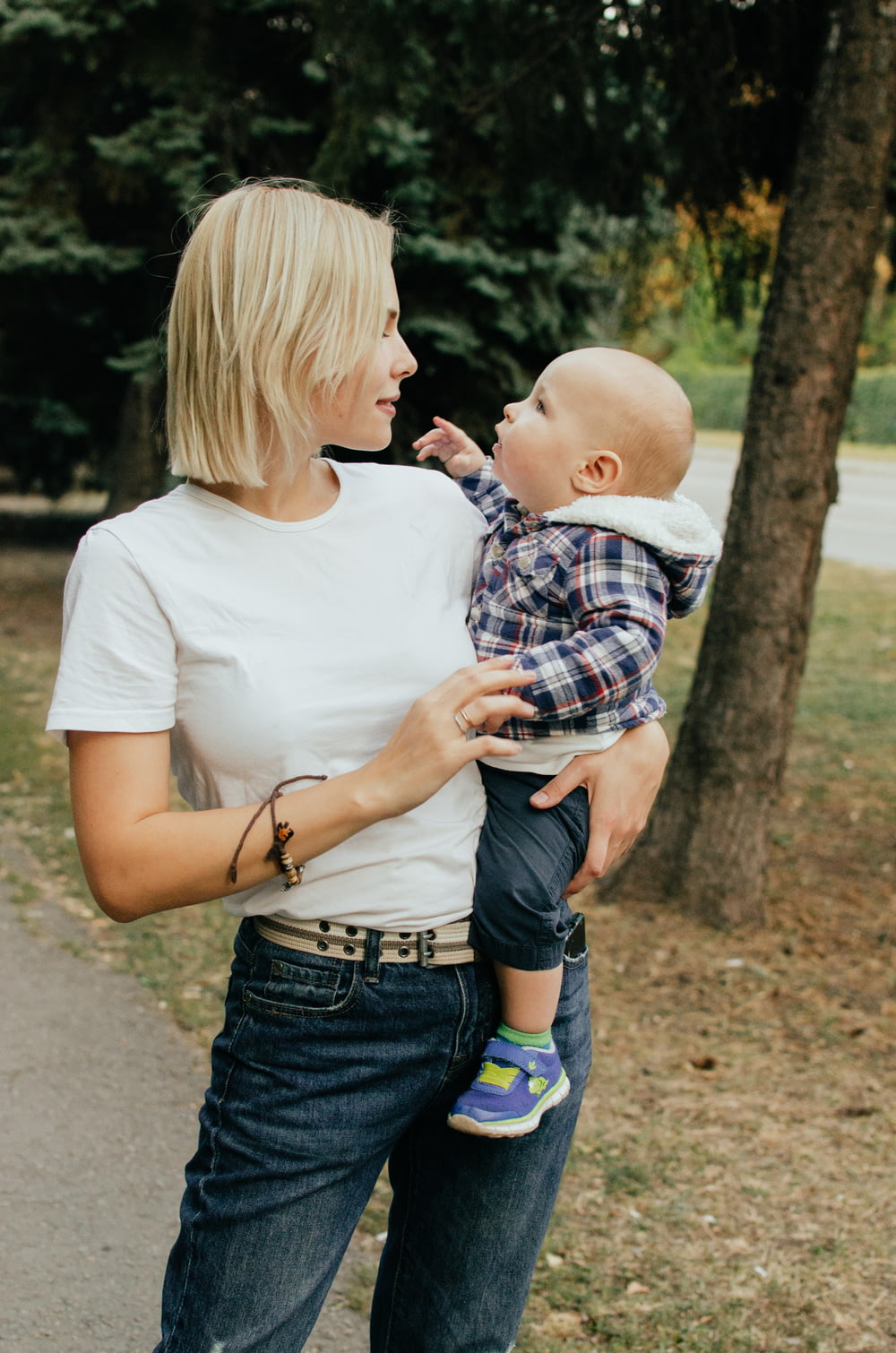 woman in white shirt carrying baby in blue and white plaid shirt