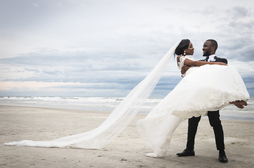 bride and groom kissing on beach during daytime