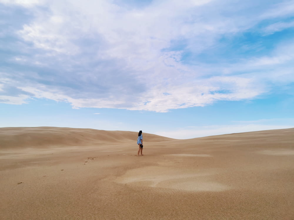 persona in giacca nera che cammina sulla sabbia marrone sotto il cielo blu durante il giorno