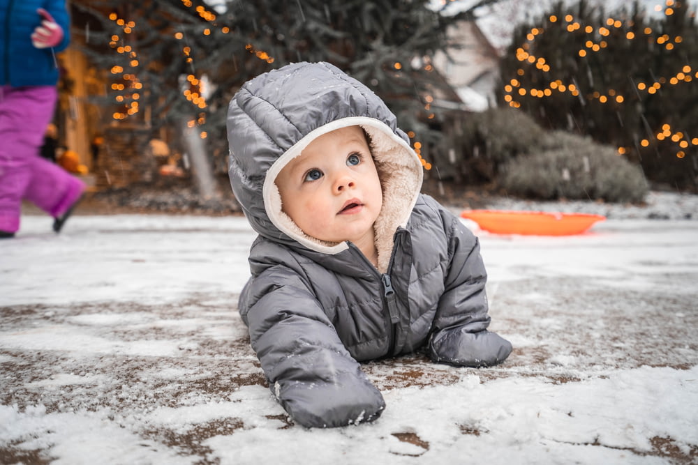 Kind in grauer Winterjacke liegt auf schneebedecktem Boden