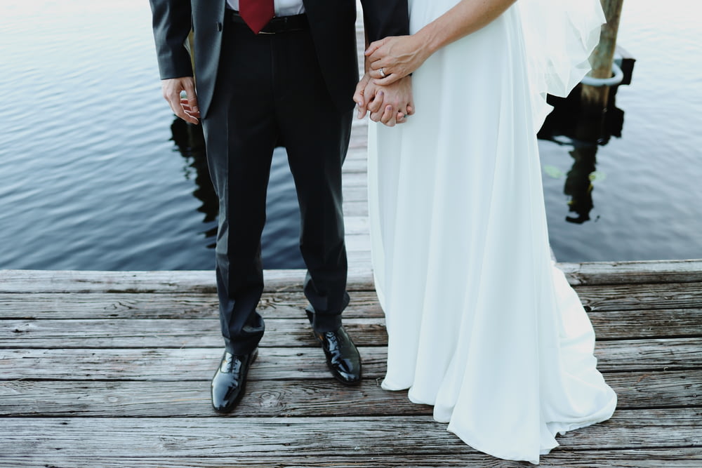 man and woman holding hands while walking on wooden dock