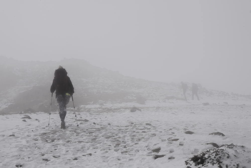 mulher na jaqueta preta que anda no campo coberto de neve durante o dia