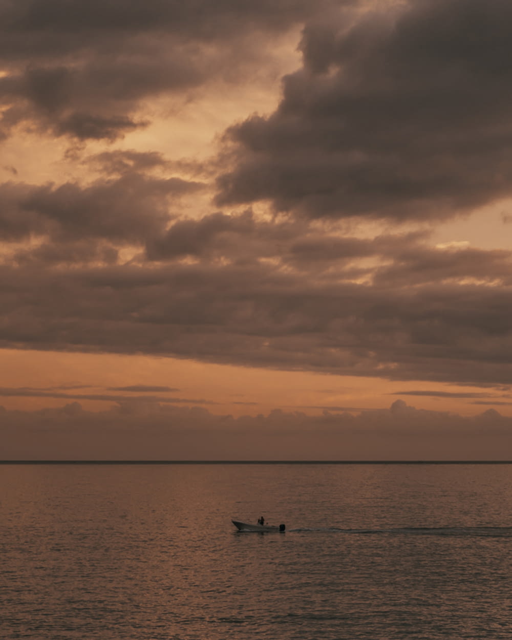 silhouette of 2 people riding boat on sea under cloudy sky during daytime