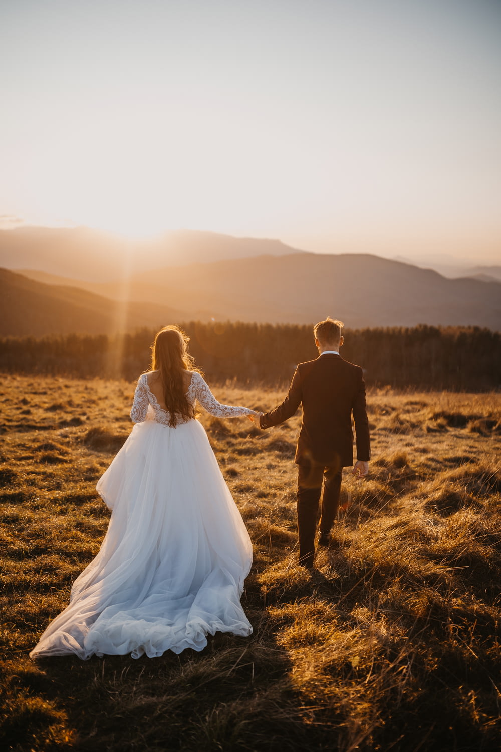 웨딩 드레스를 입은 남자와 여자는 낮 동안 갈색 잔디밭을 걷고 있습니다.
