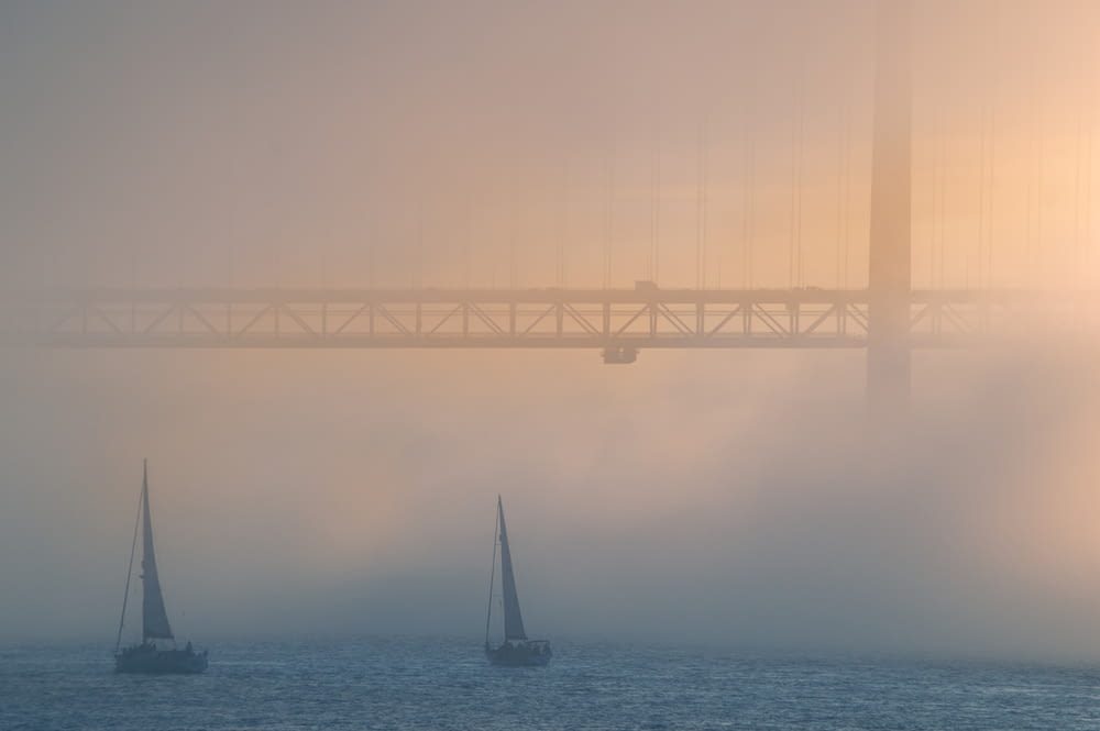 sailboat on sea under bridge during foggy day