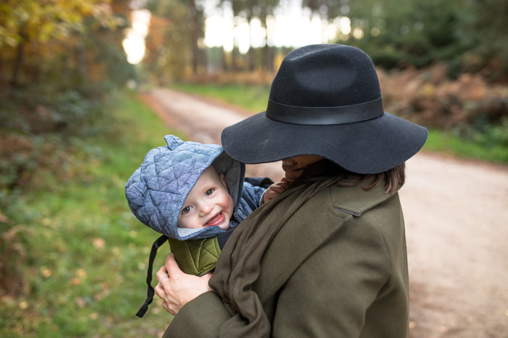 Mujer con abrigo marrón que lleva al bebé con gorro de punto azul