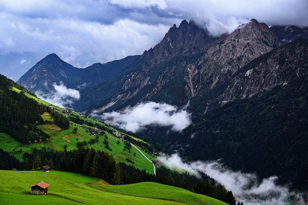 green grass field and mountains under white clouds and blue sky during daytime