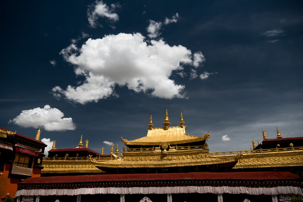 gold and red temple under white clouds and blue sky during daytime