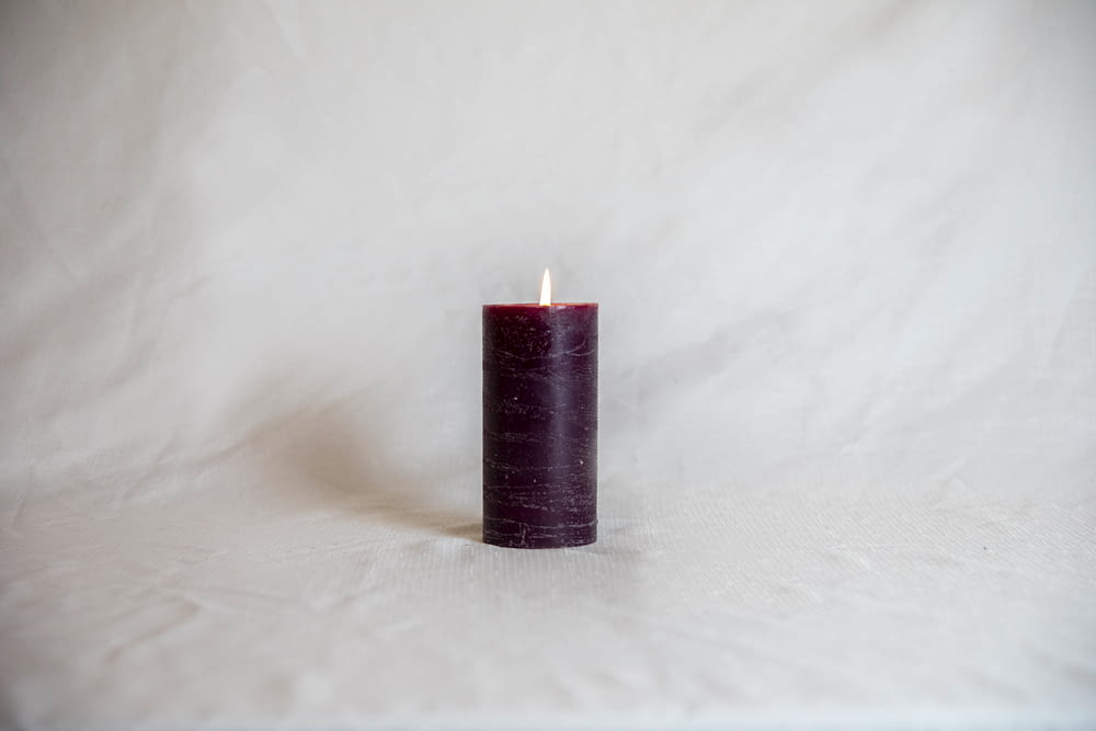 red pillar candle on white textile