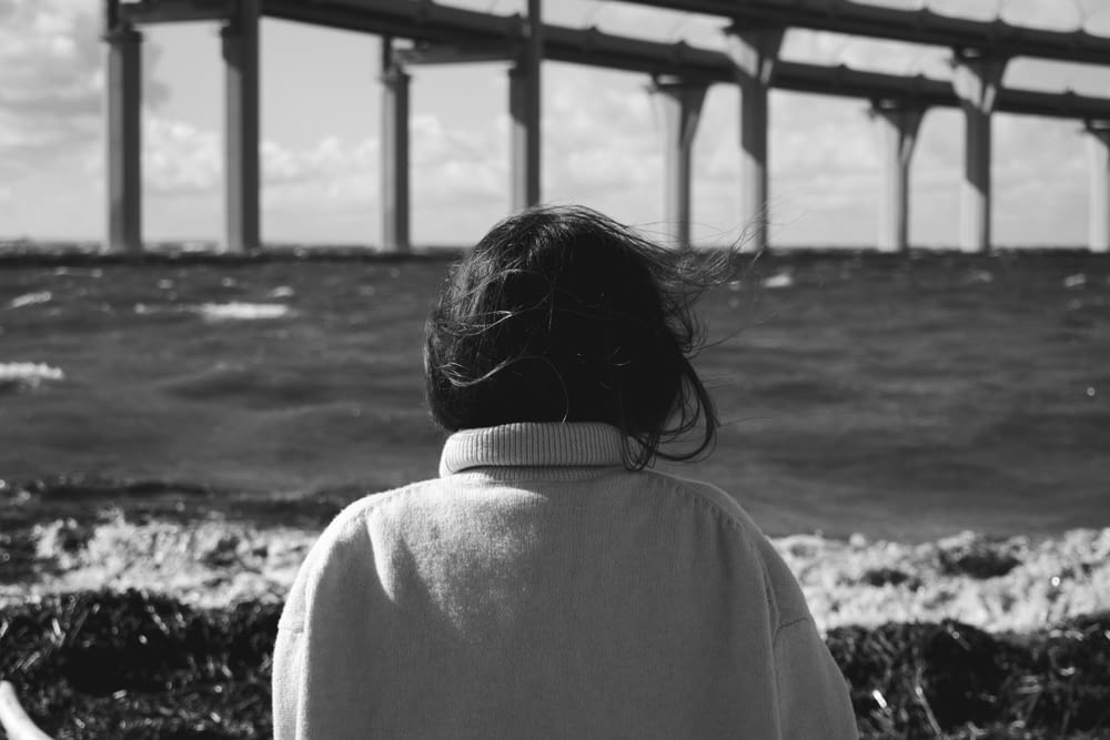 grayscale photo of woman in white shirt standing under bridge