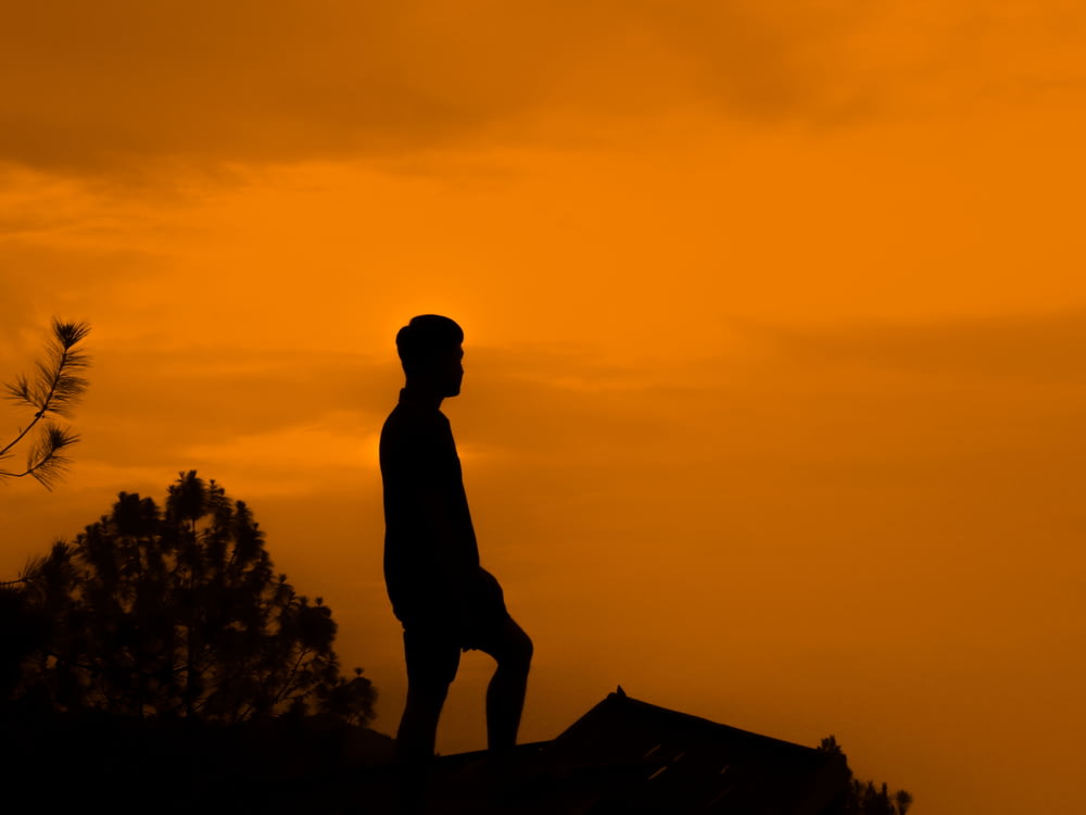 silhouette d’homme debout sur le rocher pendant le coucher du soleil