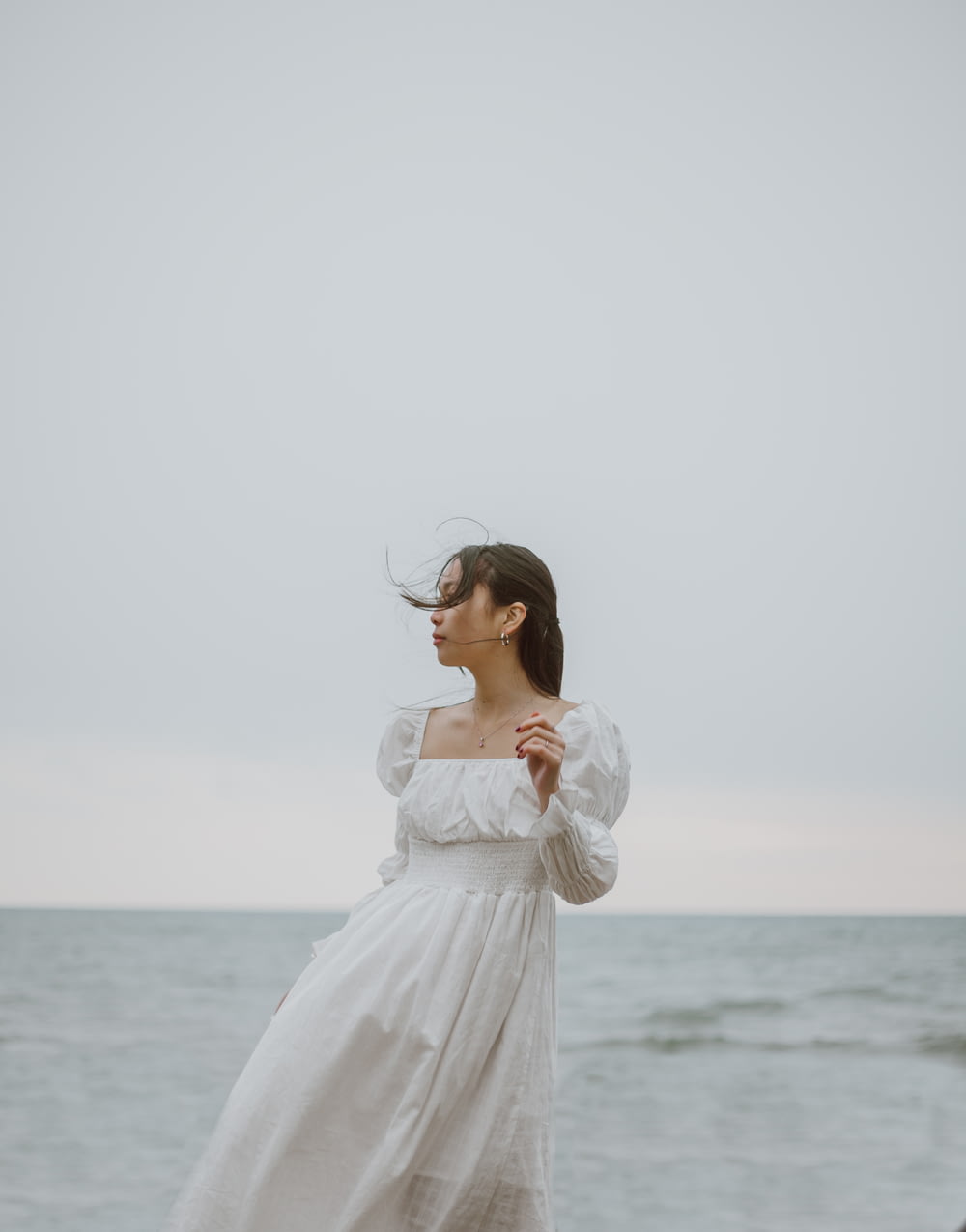 woman in white long sleeve dress standing on seashore during daytime