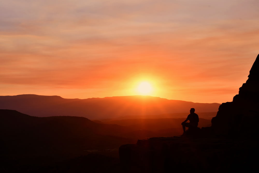 silhouette of man sitting on rock during sunset