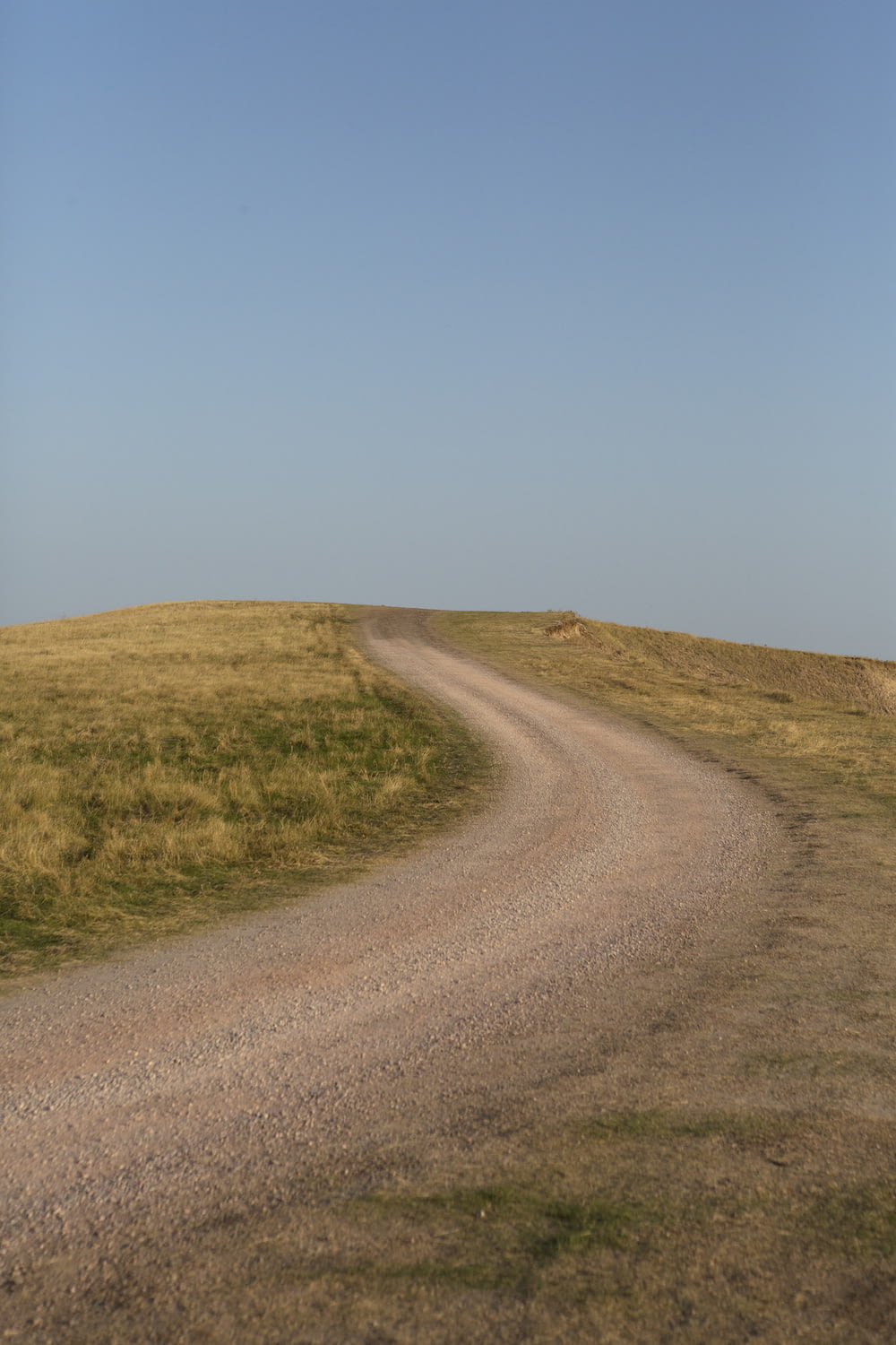 estrada de terra cinza entre o campo de grama verde sob o céu azul durante o dia