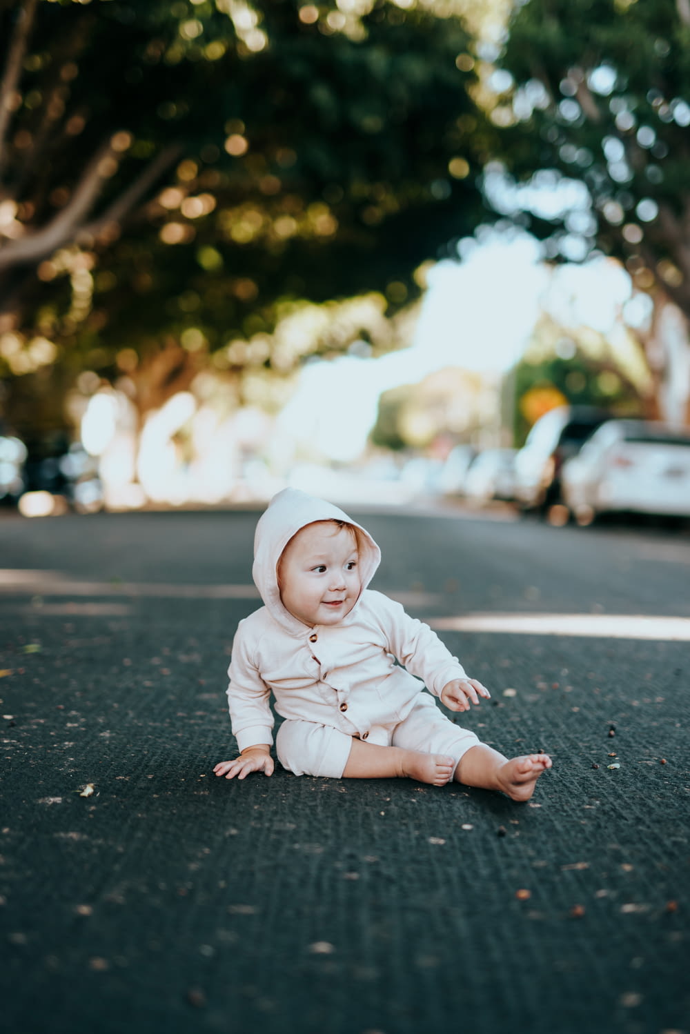baby in white onesie sitting on black asphalt road during daytime