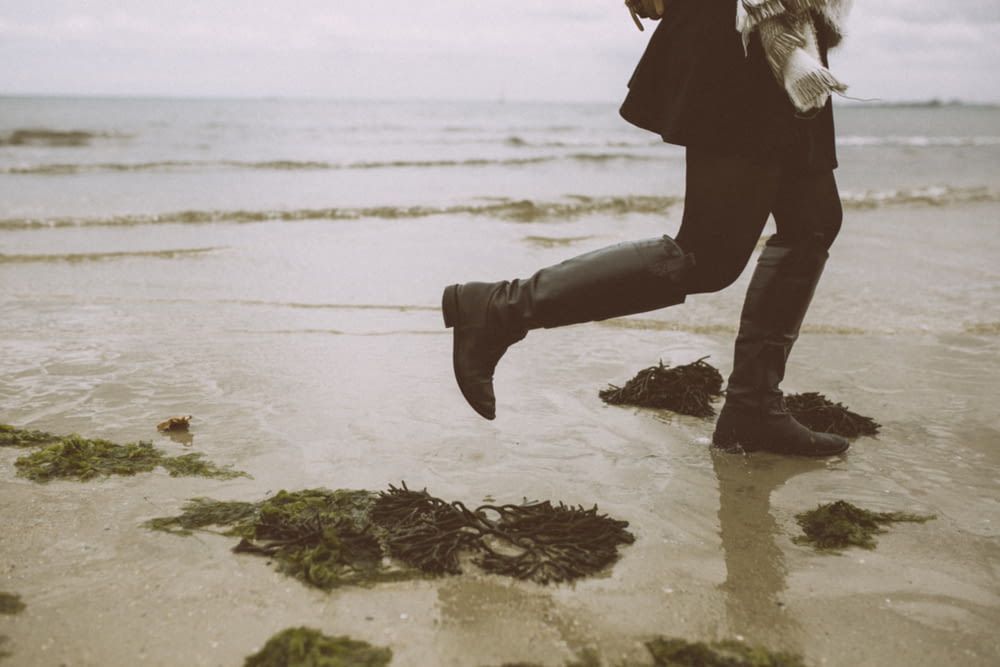 person in black pants and boots standing on beach shore