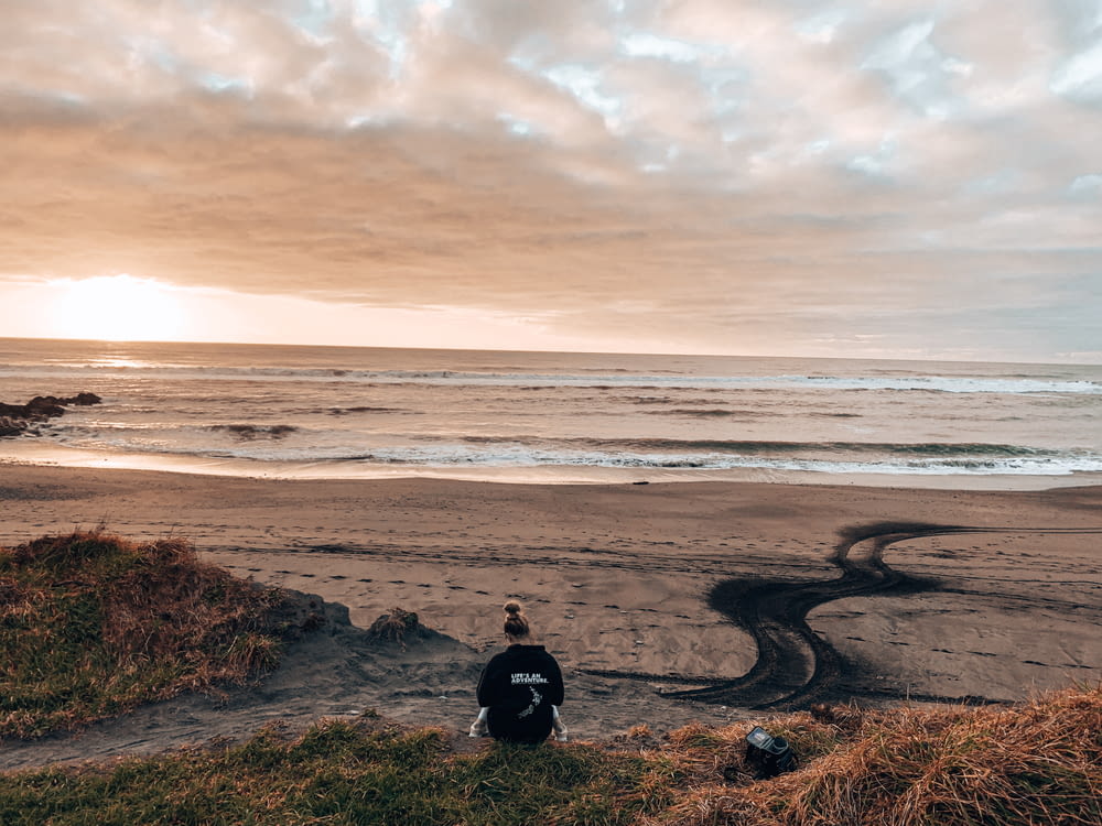 personne en veste noire assise sur un rocher brun près de la mer pendant la journée