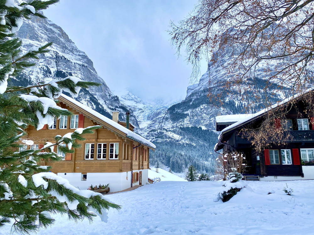 brown wooden house on snow covered ground near snow covered mountain during daytime