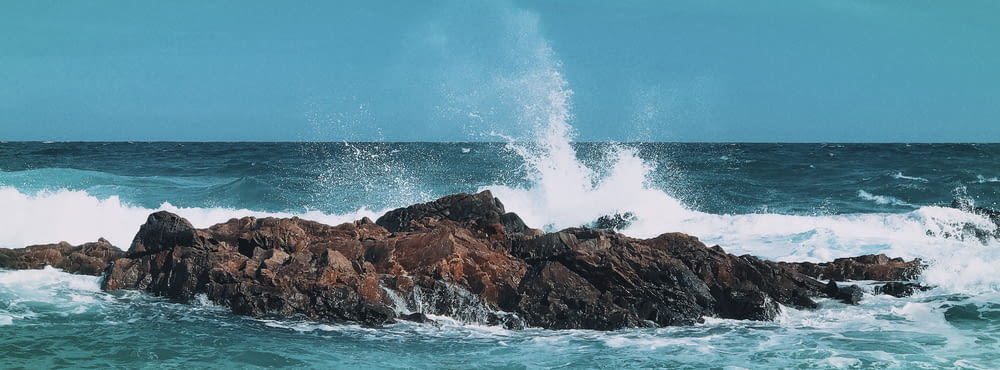 ocean waves crashing on brown rock formation under blue sky during daytime