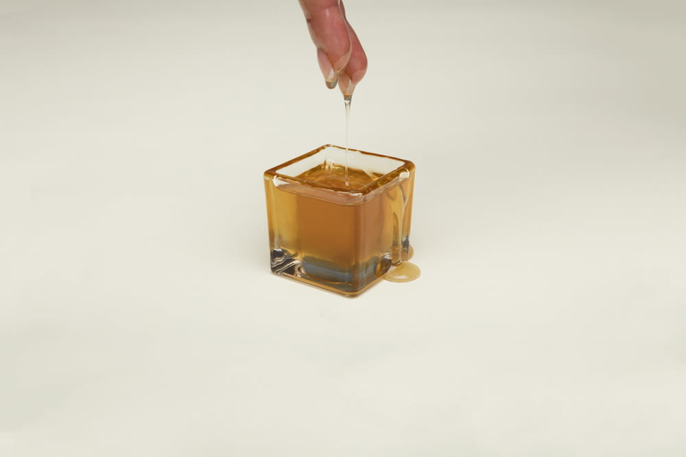 person holding clear glass container with brown liquid
