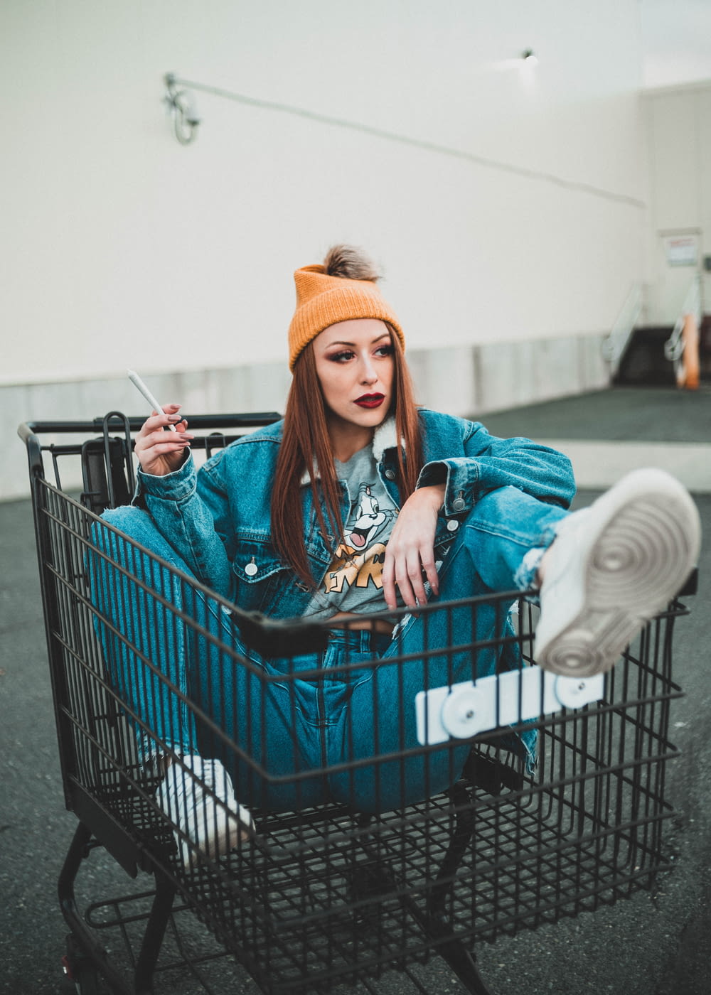 woman in blue jacket and orange knit cap sitting on shopping cart