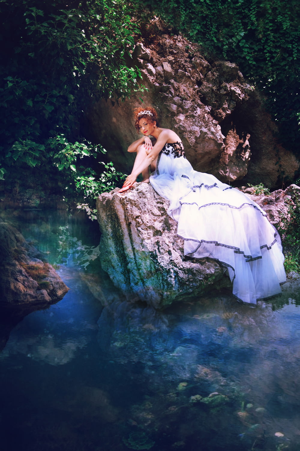 Frau im weißen Kleid sitzt auf Felsen im Wasser