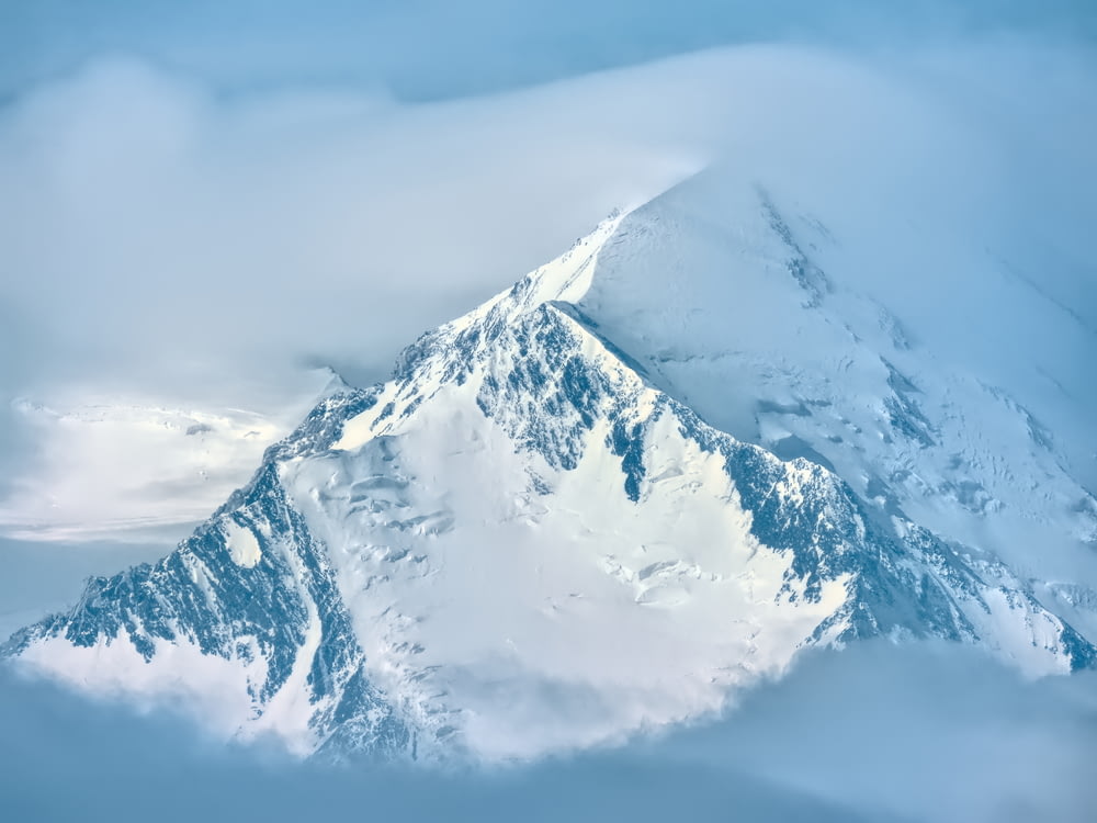 Schneebedeckter Berg tagsüber unter weißen Wolken