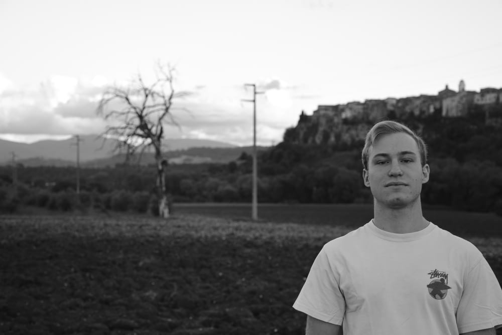 grayscale photo of man in crew neck t-shirt standing on grass field