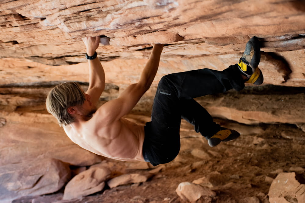 man in white tank top and black pants climbing on brown rock formation during daytime