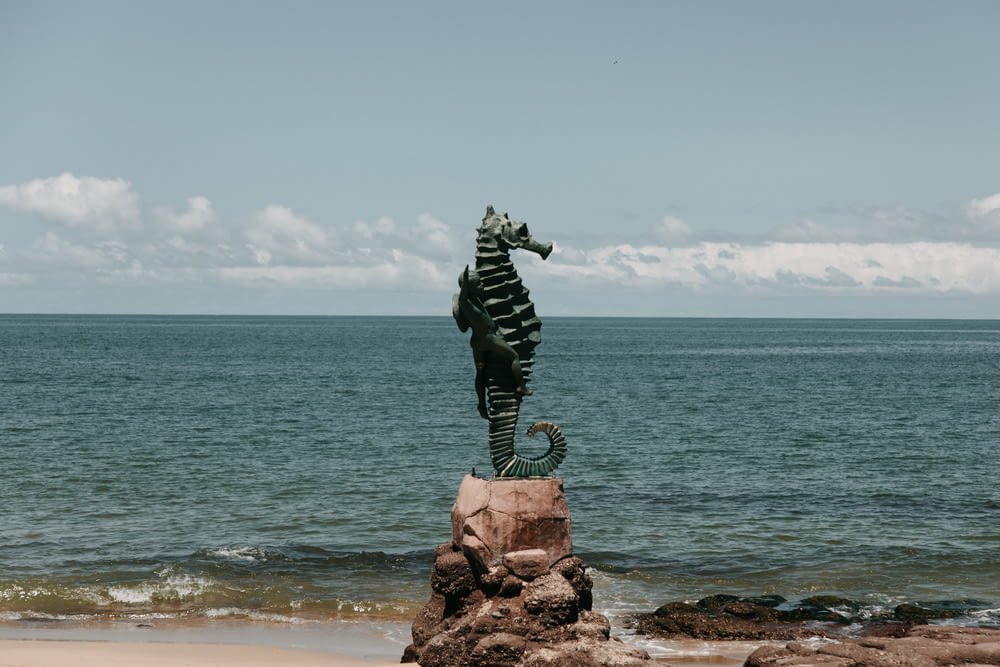 statue of man on rock formation near sea under blue sky during daytime