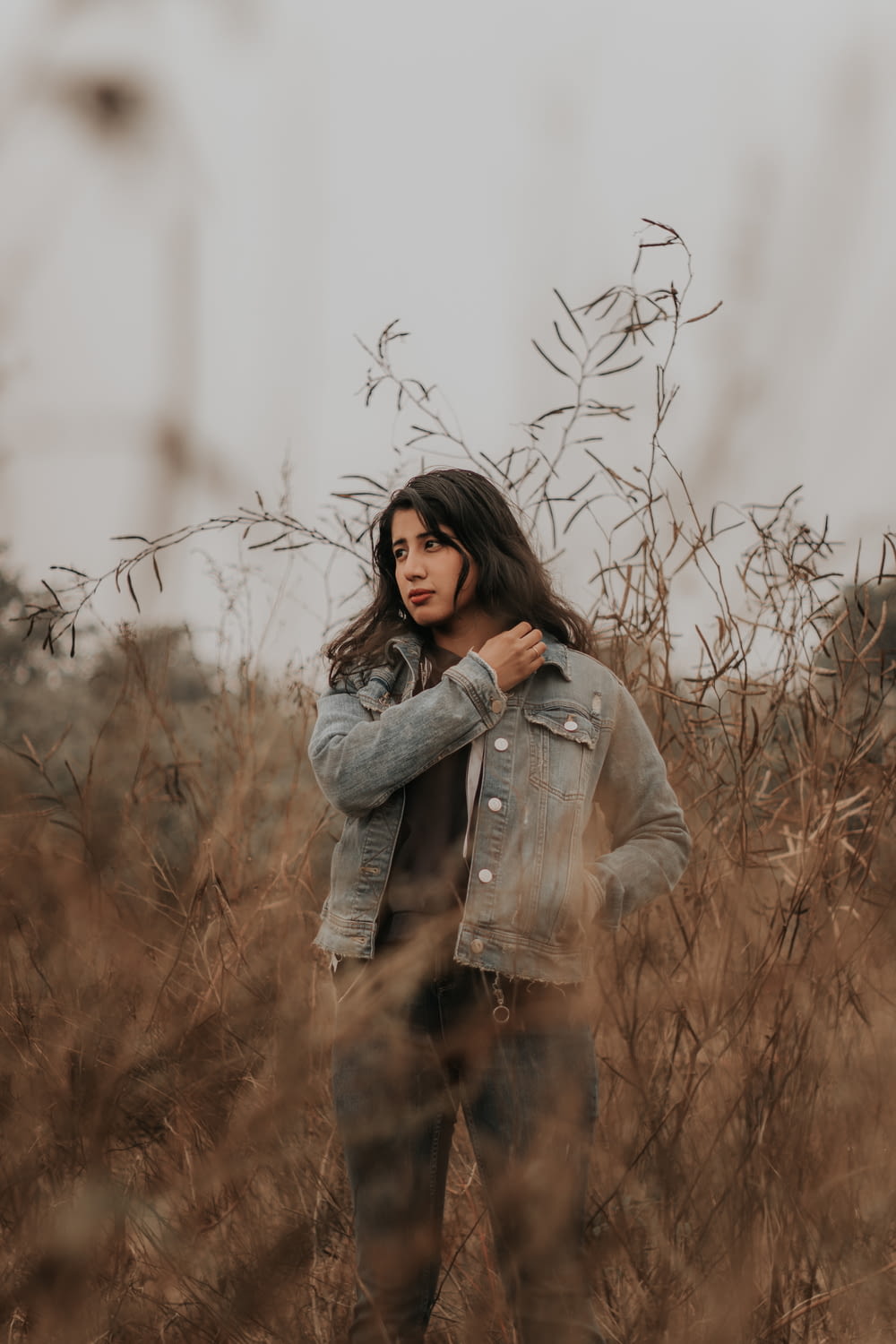 woman in gray denim jacket standing on brown grass field during daytime