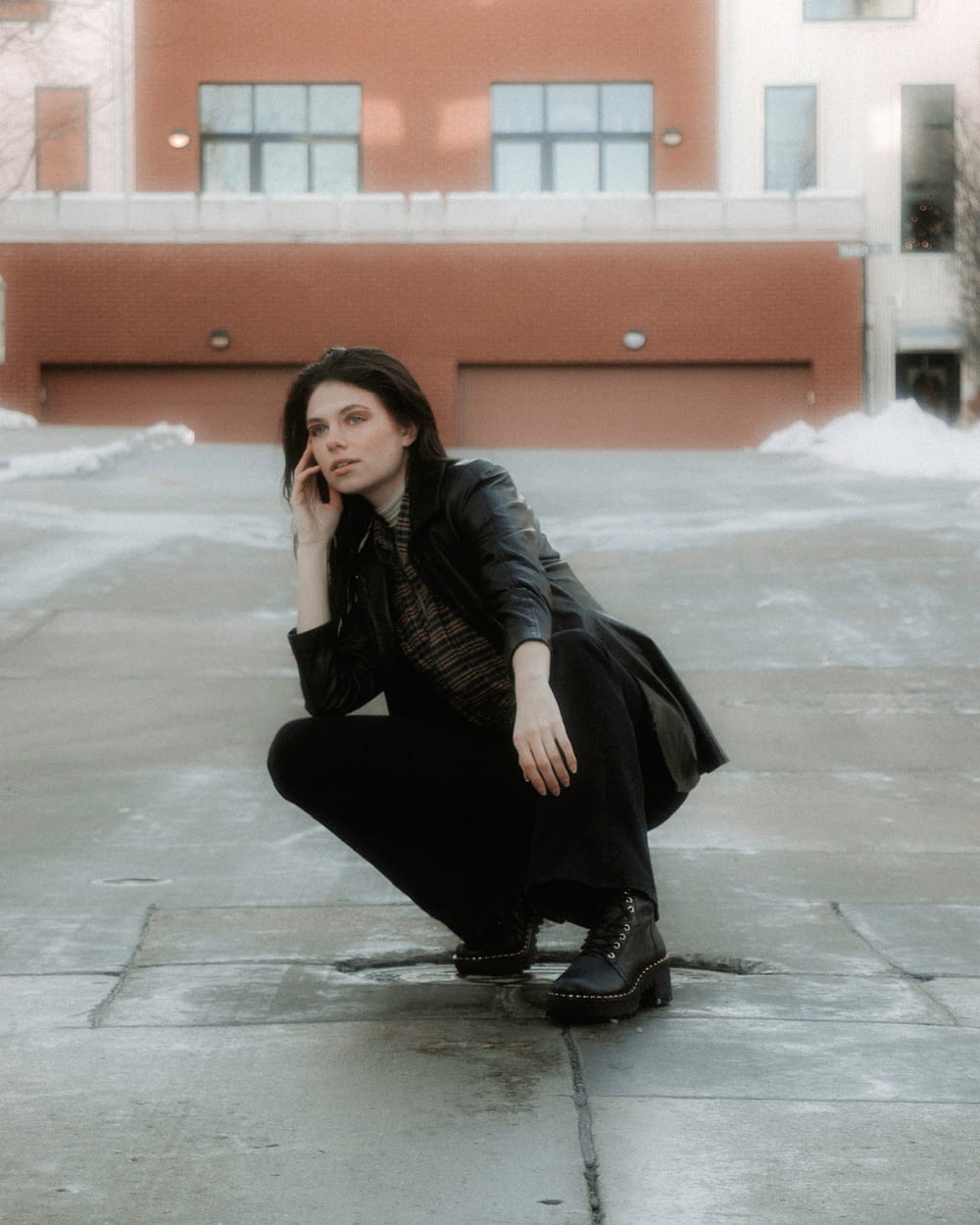 woman in black leather jacket and black pants sitting on gray concrete floor