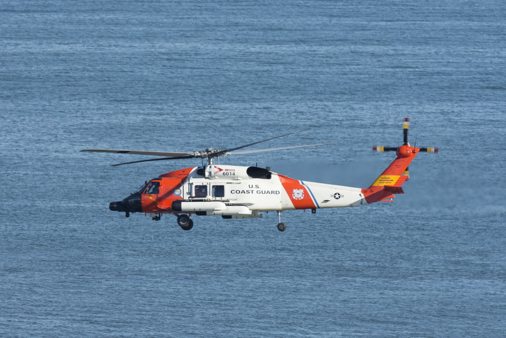 white and orange helicopter flying over the sea during daytime