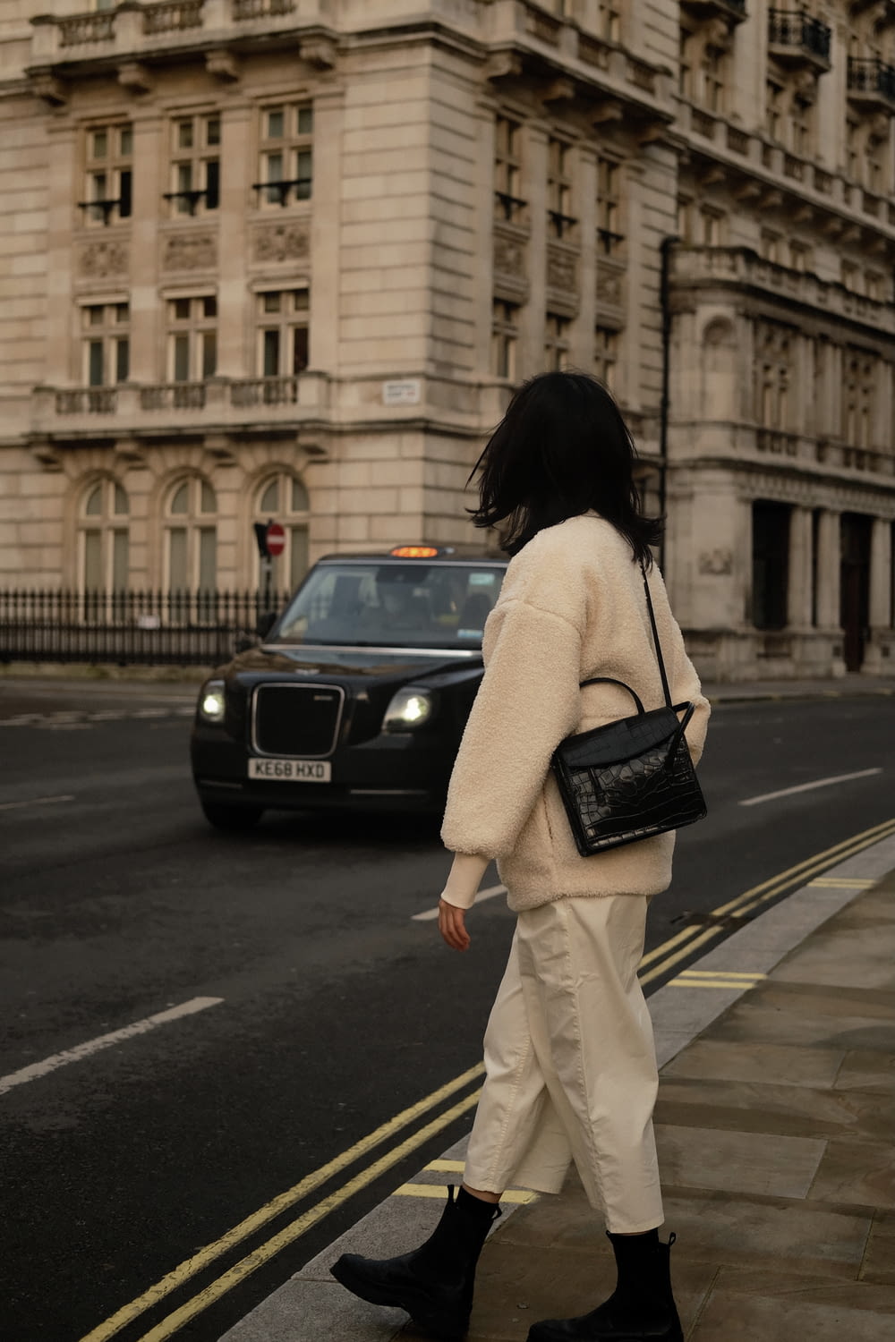 woman in white long sleeve shirt and white pants holding black leather handbag walking on pedestrian