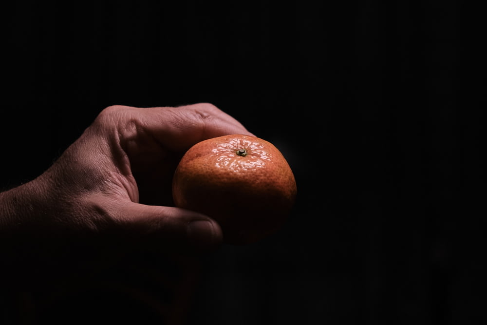 person holding orange fruit in dark room