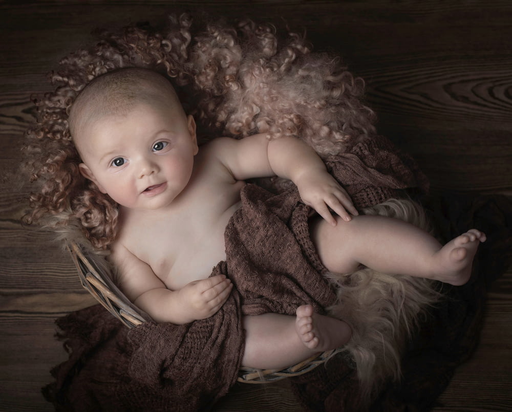 baby lying on brown textile