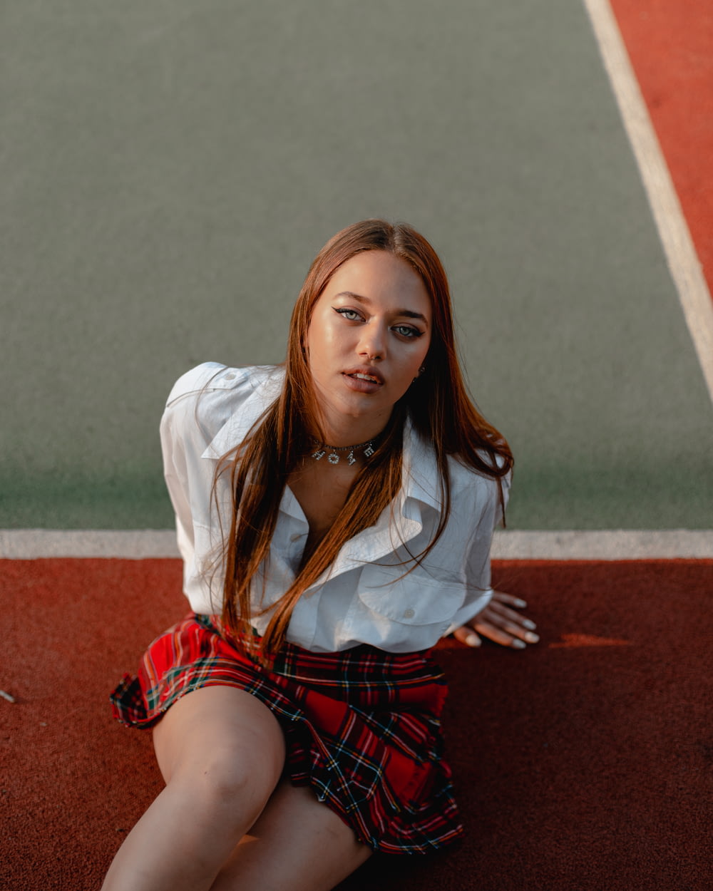 woman in white long sleeve shirt and red skirt sitting on concrete floor