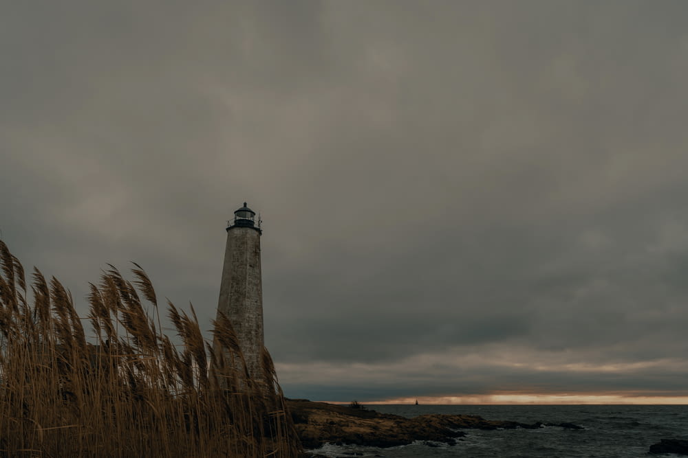 white and brown lighthouse near body of water under gray clouds
