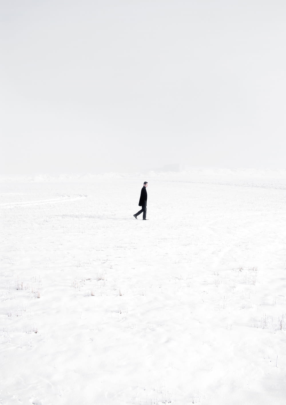 pessoa em casaco preto andando no campo coberto de neve durante o dia