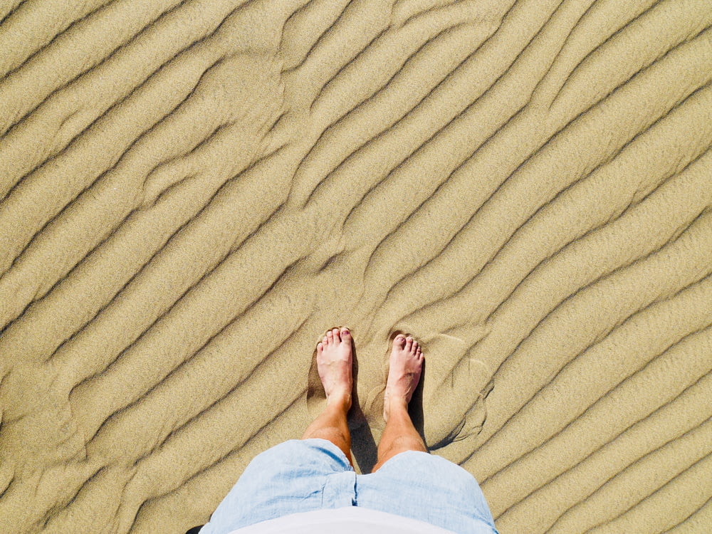 person in white pants standing on brown sand