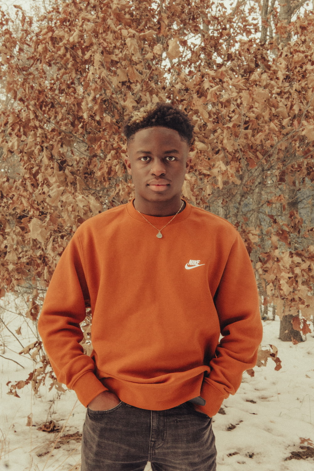 man in orange sweater standing near brown leaves