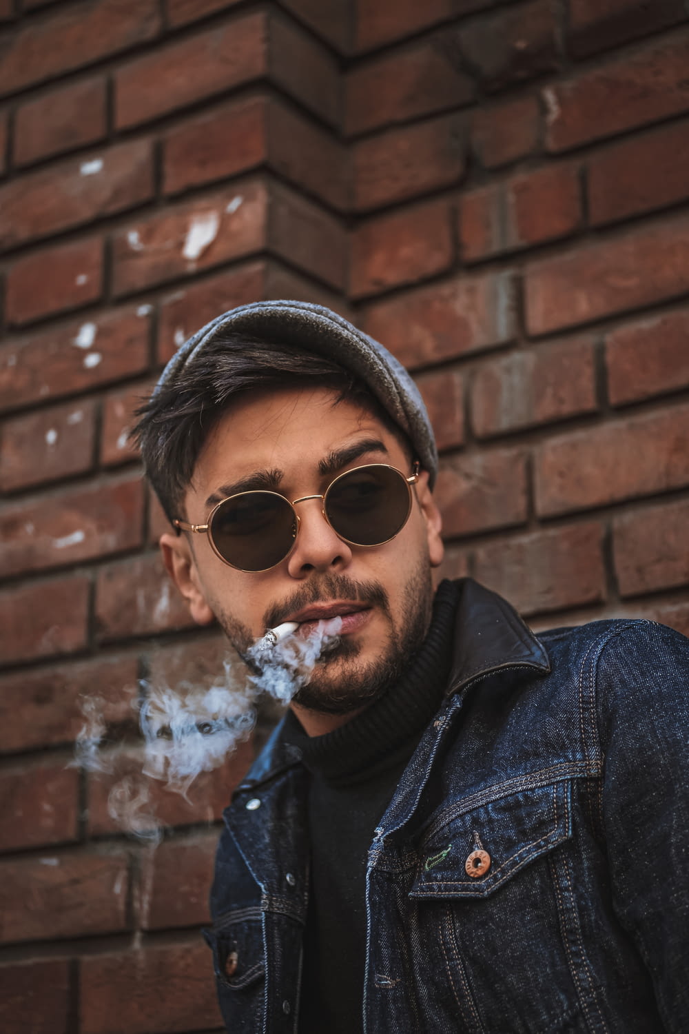 man in blue denim jacket wearing black sunglasses and black hat smoking cigarette