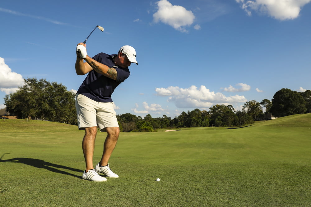 Hombre con camisa negra y pantalones cortos blancos jugando al golf durante el día