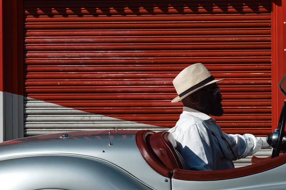 man in white dress shirt wearing brown fedora hat sitting on white car