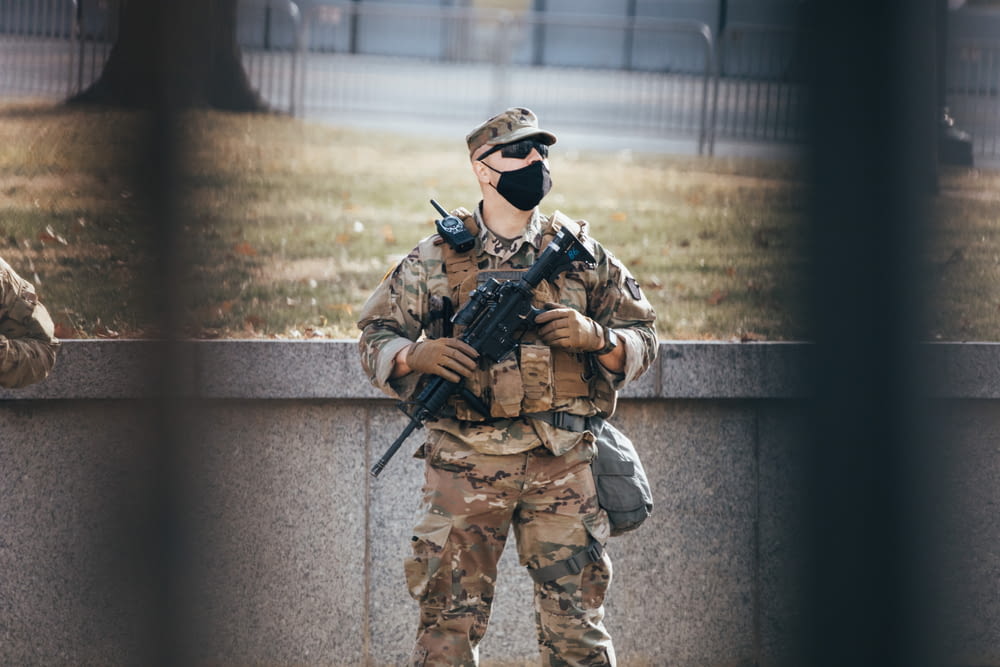 homem em uniforme de camuflagem marrom e preto segurando rifle