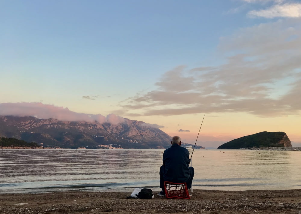 uomo in giacca nera che si siede sulla canna da pesca rossa e bianca durante il giorno