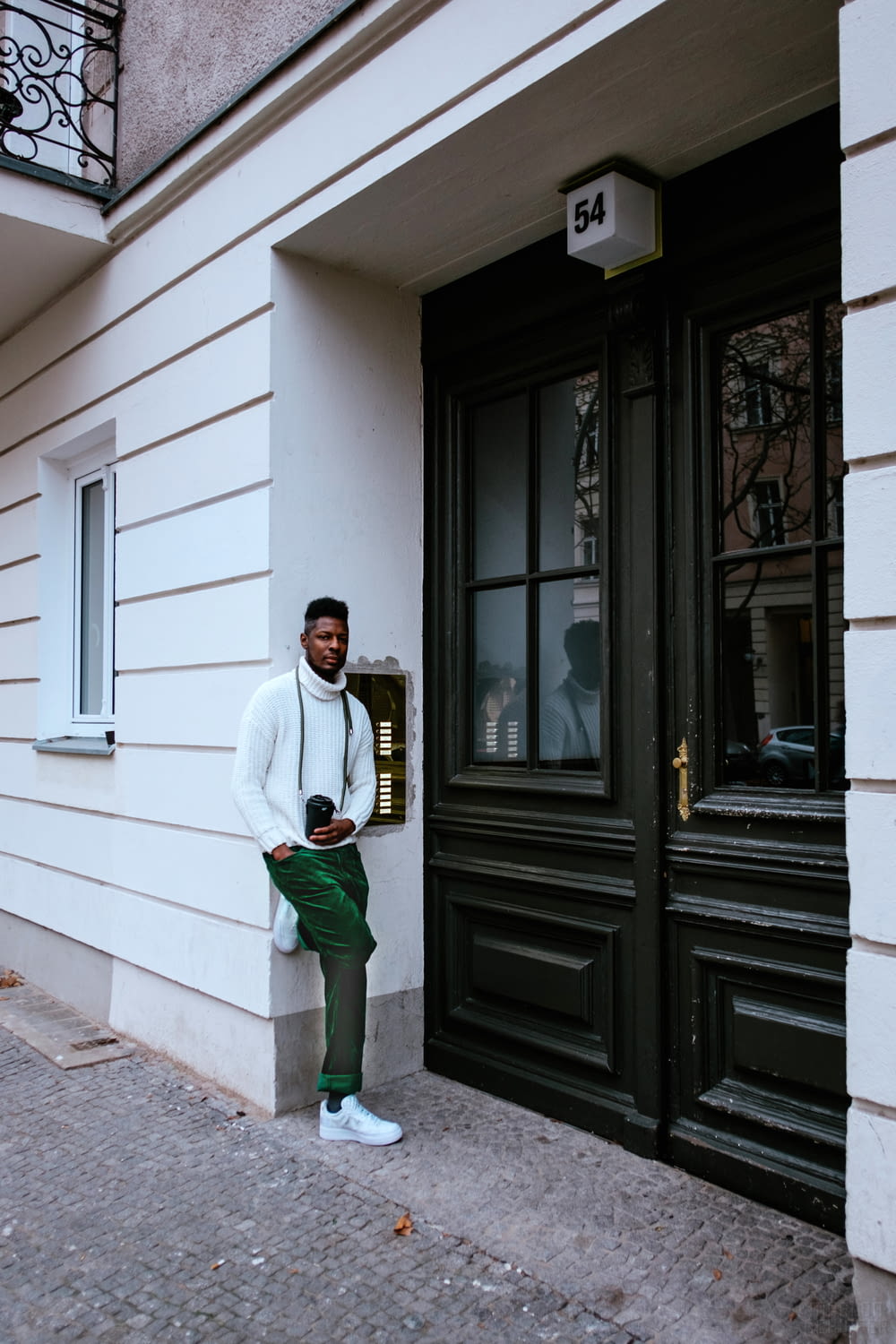 man in white dress shirt and green pants standing beside brown wooden door
